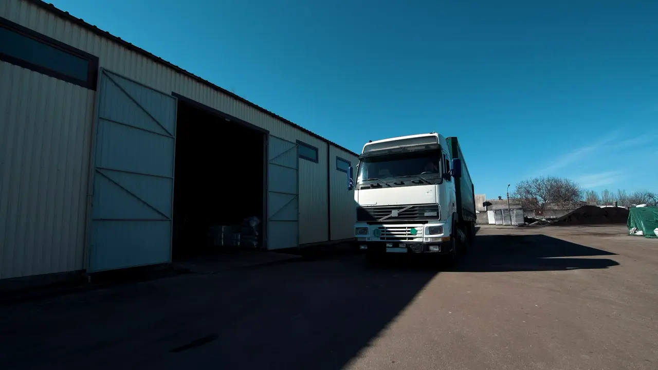Camião branco com semirreboque a sair do pavilhão de um armazém